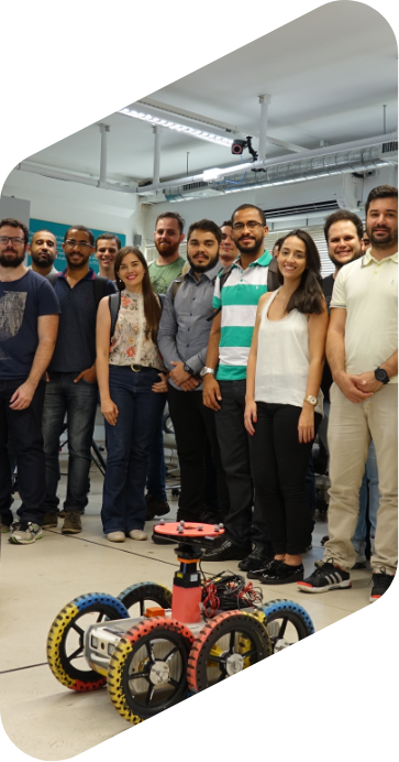 Time de estudantes do programa de mestrado Instrumentação, Controle e Automação de Processos de Mineração em pé sorrindo para foto. Na frente deles, há um robô chamado EspeleoRobô.