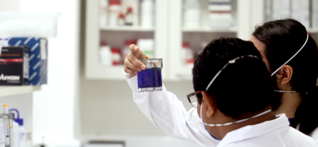 Dois pesquisadores em um laboratório olhando para um recipiente com líquido azul que um deles segura.
