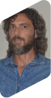 Retrato de Luciano Costa, homem de cabelo grande e barba, ambos de cor castanha. Ele está com uma expressão séria e usa uma camisa jeans.