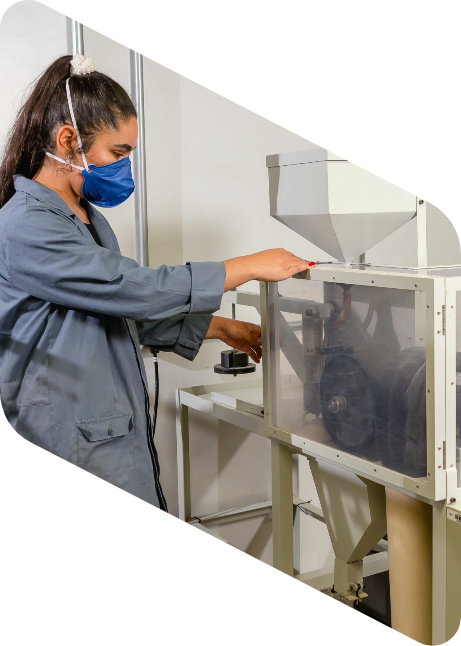 Mulher com cabelos longos presos, jaleco e máscara de cor azul operando um maquinário em um laboratório.