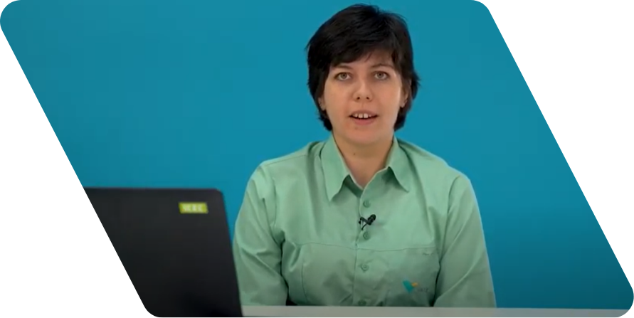 Mulher branca de cabelos lisos pretos e curtos olhando para a câmera. Ele usa uma camisa de cor verde clara e está na frente de uma parede azul.