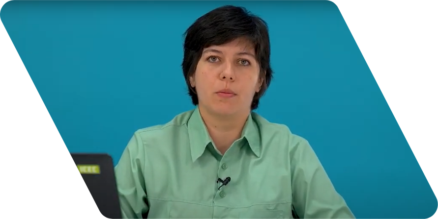 Mulher branca de cabelos lisos pretos e curtos olhando para a câmera. Ele usa uma camisa de cor verde clara e está na frente de uma parede azul.