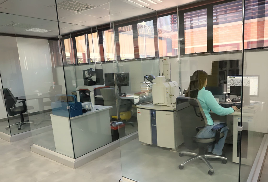 Mulher sentada em uma cabine de vidro, operando um computador e um grande equipamento de laboratório.