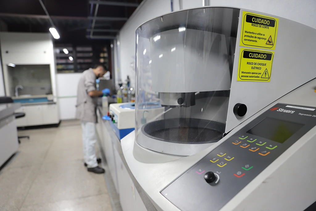Equipamento de análise de materiais no laboratório, com um pesquisador trabalhando ao fundo.