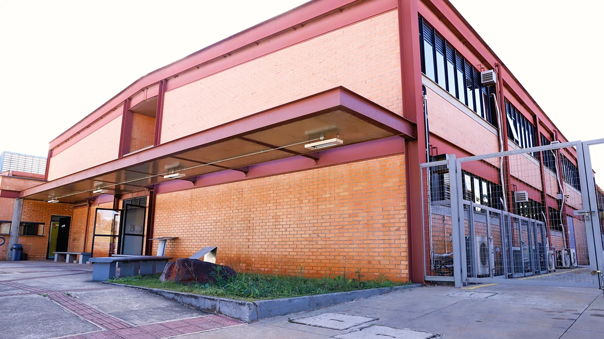 Vista de baixo para cima do edifício do ITV Mineração em tijolos laranjas e estruturas metálicas, com grandes janelas e portão na lateral.